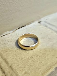 a gold wedding ring sitting on top of a cement floor next to a white wall