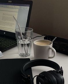 a laptop computer sitting on top of a desk next to headphones and a cup of coffee