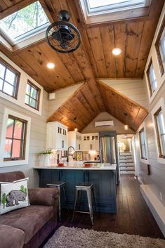 a living room and kitchen area in a tiny house with wood ceilings, hardwood flooring and skylights