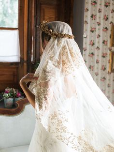 the back of a bride's wedding dress in front of a window with floral wallpaper