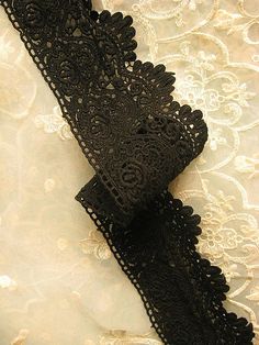 a black lace garter with an intricate design on it's edge, laying on a white fabric