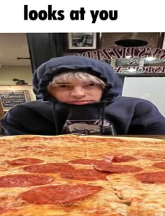 a young boy sitting in front of a large pepperoni pizza