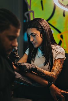 a woman getting her tattoo done by a man in front of a graffiti covered wall