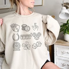 I'd Rather be at the Casino! This gambling shirt featuring a lucky 7 ball, shamrock, horseshoe and other lucky charms would be perfect for a casino theme party, casino retirement, or gambling gift. If you or your loved one is probably at the casino, then this is the cozy, comfy sweatshirt for you!  -Unisex, heavy blend crewneck sweatshirt -Made from 50% polyester and 50% cotton -Ribbed knit collar retains shape -No itchy side seams or tags (label is sewn-in) -Loose fit is true to size  FREE SHIPPING! Printed in the USA -------SIZING------- Please consult the size chart in the listing images carefully for fit. If you want an oversized look, consider sizing 1-2 sizes up. -------SHIRT COLORS------- Please see images for different colors offered. Note: white can appear grey or faded on darker Casino Theme Party Outfit Women, Casino Theme Party, Party Outfits For Women, Lucky 7, Balls Shirt, Merch Ideas, Casino Outfit, Gambling Gift, Casino Theme