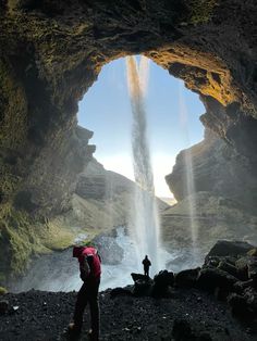 two people standing in front of a cave with water coming out from the entrance to it