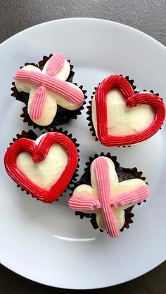 four cupcakes with red and white frosting in the shape of hearts on a plate