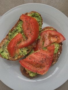 two pieces of toast with tomatoes and avocado on it sitting on a white plate