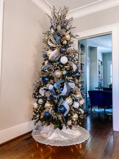 a decorated christmas tree with blue and silver ornaments in a living room next to a doorway