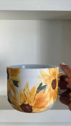 a hand holding a coffee cup with sunflowers painted on it