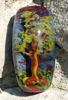 a painted glass object sitting on top of a rocky ground next to a rock wall