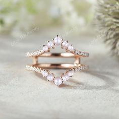 an open ring with pink pearls and white diamonds on it, sitting next to a pine tree