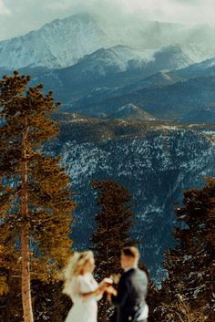 a bride and groom standing on top of a snow covered slope in front of mountains