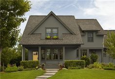 a gray house with black shutters on the front door and green grass in front