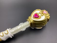 a gold and white toy with a pink heart on it's handle, sitting on a gray surface