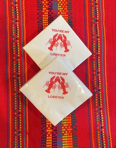 two napkins with lobster designs on them sitting on a red and blue table cloth