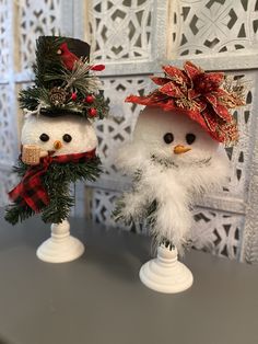 two snowmen wearing hats and scarfs on top of each other in front of a white wall