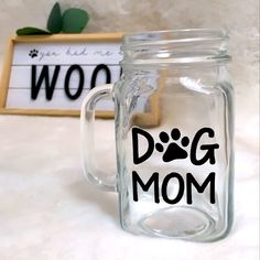 a glass mug with the words dog mom on it next to a sign that says woo