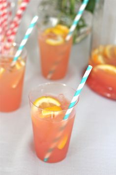 three glasses filled with orange juice and two straws on the table next to each other