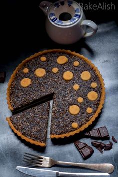 a chocolate tart pie with pieces cut out on a table next to a teapot