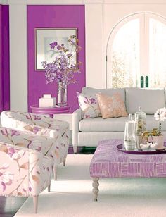 a living room with white furniture and purple accents on the walls, along with flowers in vases