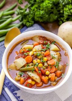 a white bowl filled with vegetable soup next to potatoes and broccoli on a blue towel