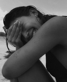 a black and white photo of a woman sitting on the beach with her eyes closed