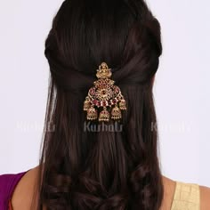 a woman with long dark hair wearing a gold and red brooch on her head