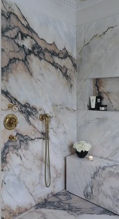 a white and black marble bathroom with gold faucet, shower head and hand shower