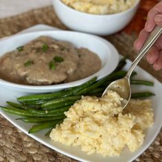 a person is spooning mashed potatoes and green beans with gravy on the side