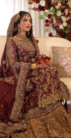 a woman in a red and gold bridal gown sitting on a couch with flowers