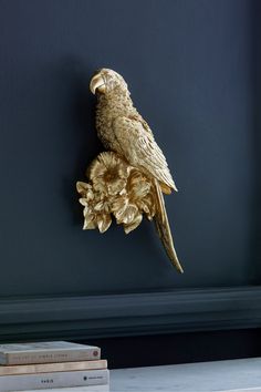 a gold bird is perched on top of a branch with flowers in front of a blue wall