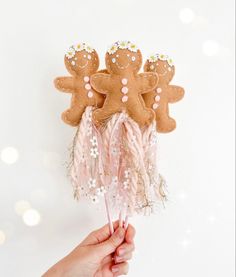 a hand holding two gingerbreads with pink feathers and white daisies on them