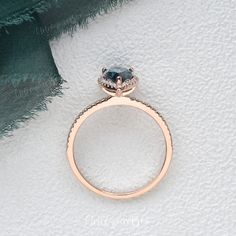 an engagement ring with a blue diamond on it and a green scarf in the background