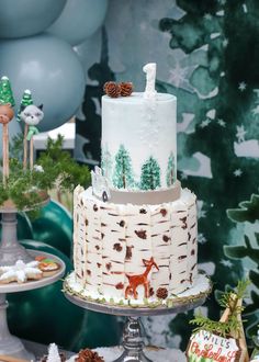 a three tiered cake with white frosting and pine cones on top, surrounded by other desserts