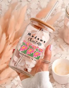 a person holding a jar filled with marshmallows next to a cup of coffee