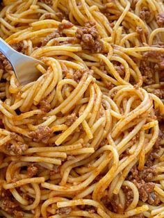 a spoon full of spaghetti with meat and sauce on the top, in a skillet