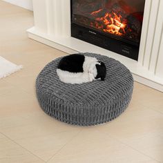 a black and white cat curled up on a round bed in front of a fireplace