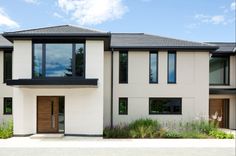 two story white house with black trim and wood doors on the second floor, surrounded by greenery