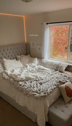 an unmade bed in front of a window with lights on the wall and curtains