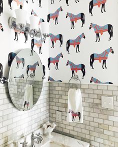 a bathroom with horses on the wall next to a white sink and mirror in front of a brick wall