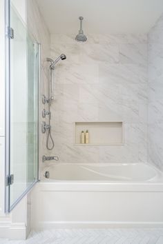 a bathroom with white marble walls and flooring, including a bathtub that has two shower heads on the wall