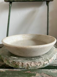 a white bowl sitting on top of a stone slab next to a green metal chair