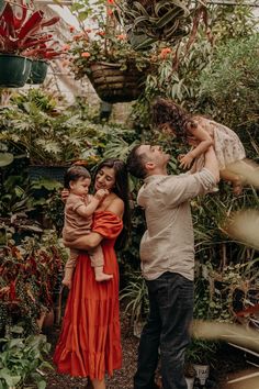 a man and woman holding two children in their arms while they are surrounded by plants