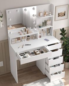 a white vanity table with drawers and makeup products on the top shelf next to a potted plant