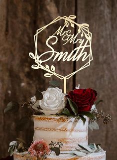 a wedding cake with white frosting and red flowers on top is sitting on a wooden table