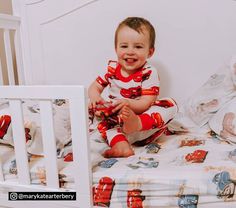 a baby sitting on top of a bed next to a white crib with sheets