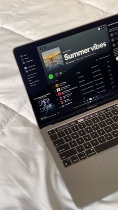 an open laptop computer sitting on top of a white bed covered in sheets and pillows