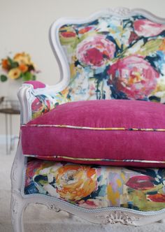 a pink pillow sitting on top of a white chair next to a vase with flowers