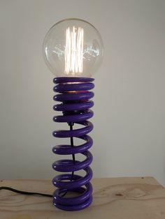 a light bulb sitting on top of a purple spiraly object with a black cord