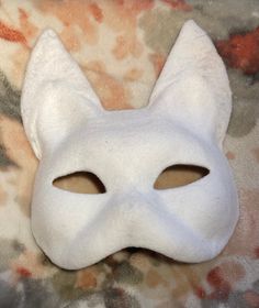 a white cat mask sitting on top of a bed